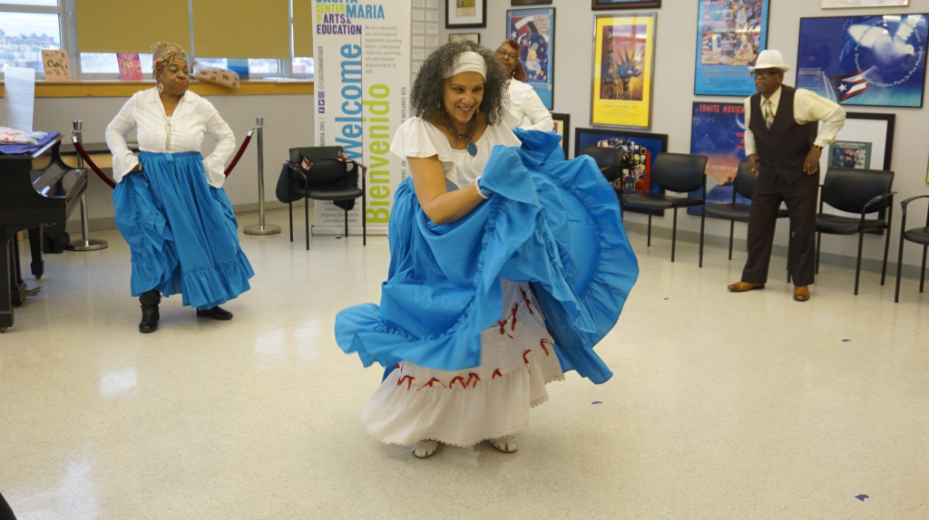 A woman dances La Bomba in a traditional ruffled blue skirt.