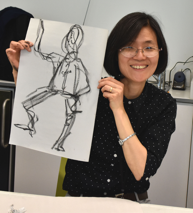 A woman is holding a black and white sketch of a human figure.