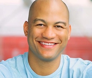 Headshot of Lifetime Arts Trainer, Clark Jackson. His head is buzzed and he has dark eyes. He is smiling.