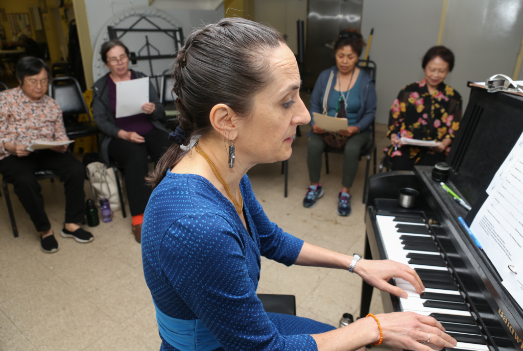 A female teaching artist accompanies her students singing on piano.